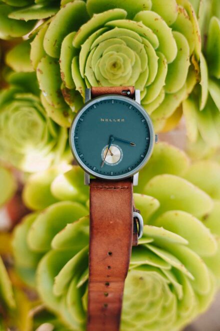 Reloj del novio, de esfera verde y correa de cuero marrón, apoyado sobre una planta suculenta
