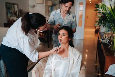 Una maquilladora le pinta los labios a la novia mientras un peluquero le echa laca en el pelo
