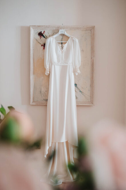 El vestido de novia, de manga de gasa con encaje en los puños, colgado delante de un cuadro