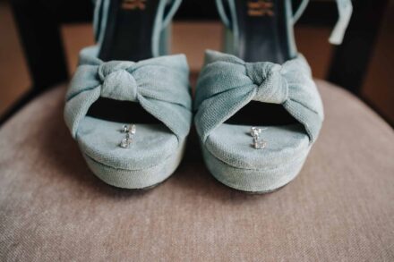 Zapatos de ante azul claro con nudo delantero, con los pendientes de la novia sobre la plantilla