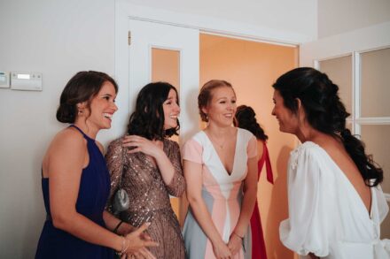 Tres invitadas se ríen al ver a la novia vestida, y una se lleva la mano al pecho