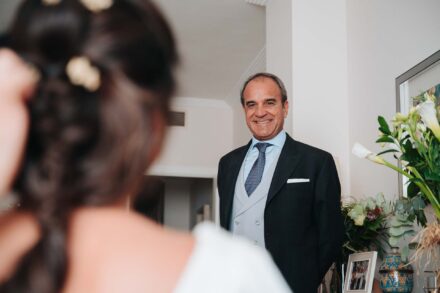 Un invitado de chaqué sonríe al ver a la novia, de espaldas y desenfocada en primer plano