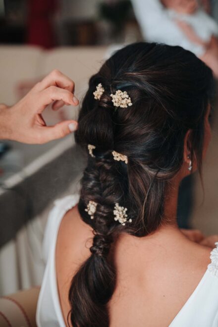 La trenza de la novia, adornada con pequeñas flores blancas, y una mano que se acerca a retocarla