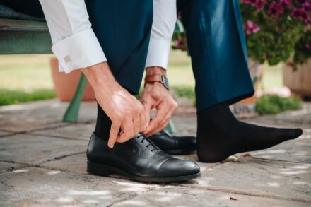 El novio se ata los cordones de los zapatos negros, sentado en un banco verde