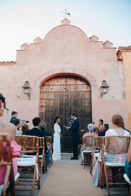 El novio habla al micrófono frente a la novia ante la fachada con veleta de Hacienda Los Molinillos (Sevilla)