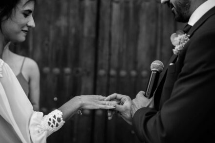 En blanco y negro, el novio pone el anillo a la novia con el micrófono en la otra mano
