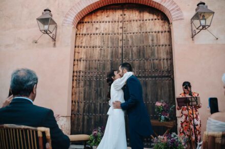 Los novios se besan ante el portón de madera mientras los invitados aplauden