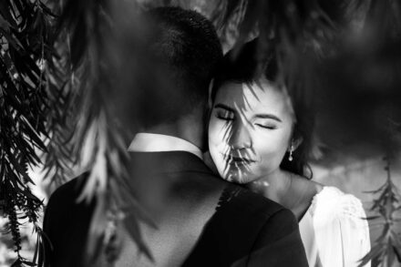 En blanco y negro, la novia cierra los ojos abrazada al novio, con la sombra de las hojas en la cara