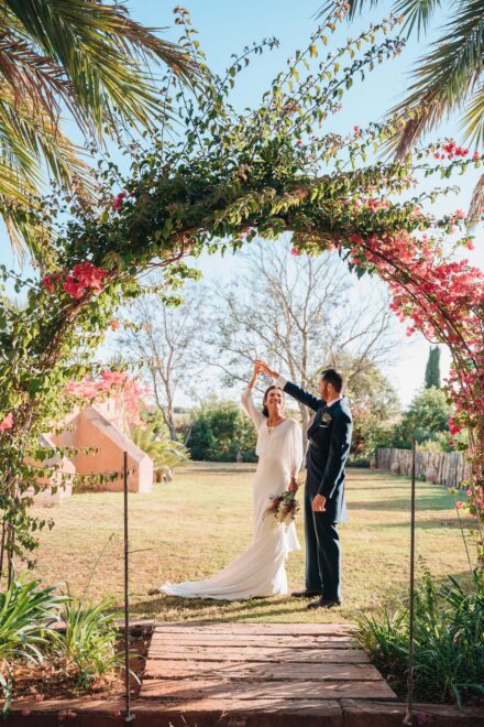 La novia gira de la mano del novio bajo un arco de buganvillas, en el jardín de Hacienda Los Molinillos (Sevilla)