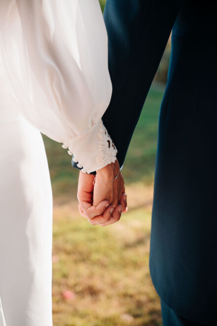 Las manos entrelazadas de los novios de cerca, con el puño de encaje de la manga de la novia