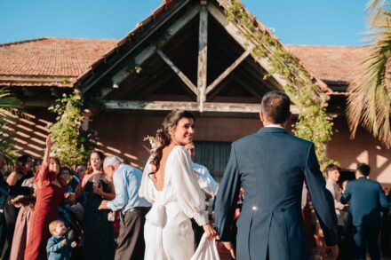 Los novios llegan de la mano entre los invitados, que aplauden, frente a un porche de vigas de madera