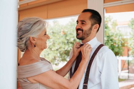 Una invitada de pelo canoso le ajusta la corbata granate al novio, y los dos sonríen