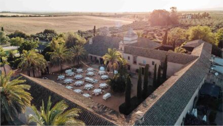 Vista aérea de Hacienda Los Molinillos (Sevilla) entre campos al atardecer, con las mesas aún vacías en el patio