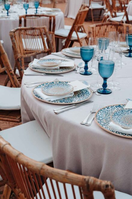 Una mesa del banquete de cerca, con platos de cerámica azul estampada, copas azules y sillas de bambú