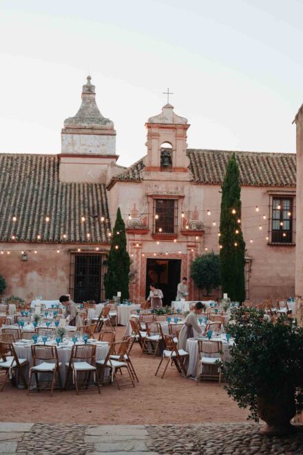 Camareros preparan las mesas del banquete en el patio, bajo la espadaña con campana de la hacienda