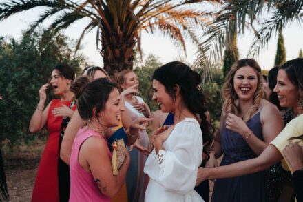La novia se ríe con la mano en el pecho, rodeada de invitadas que gritan de alegría
