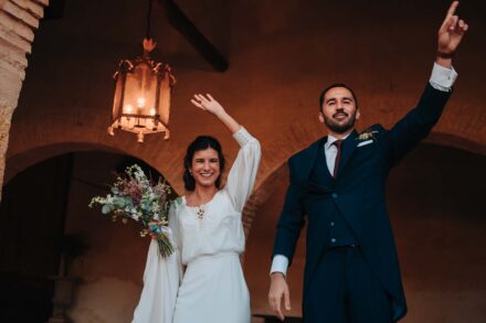 Los novios saludan con el brazo en alto bajo un farol encendido, en un soportal de arcos