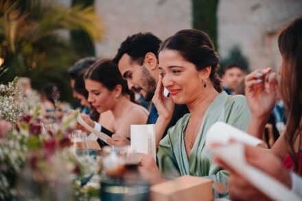 Una invitada emocionada se seca una lágrima mientras lee una carta en la mesa del banquete