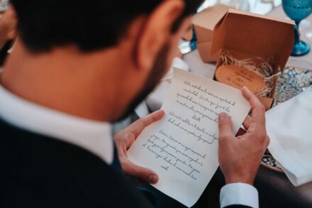 Por encima del hombro, un invitado lee una carta escrita a mano junto a una cajita de cartón abierta