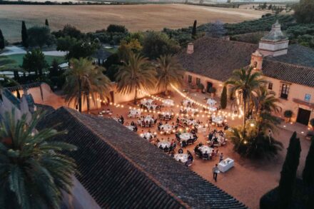 Vista aérea del patio de Hacienda Los Molinillos al anochecer, con las mesas de la cena bajo guirnaldas de luces