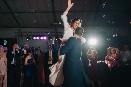El novio levanta en brazos a la novia, que alza la mano entre pompas de jabón, y los invitados aplauden