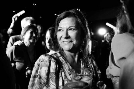 Una invitada sonríe con un vaso en la mano en medio de la fiesta, en blanco y negro