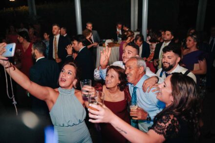 Una invitada se hace un selfi con el móvil y un grupo de invitados se asoma sonriendo a la foto
