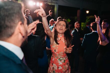 Una invitada con vestido naranja de flores baila con los ojos cerrados y un dedo apuntando arriba