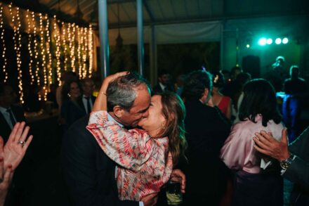 Una pareja de invitados se besa abrazada en la pista de baile, ante una cortina de luces