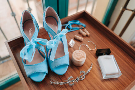 The bride’s blue bow sandals, jewelled headpiece, bracelet, perfume and ring box on a wooden tray