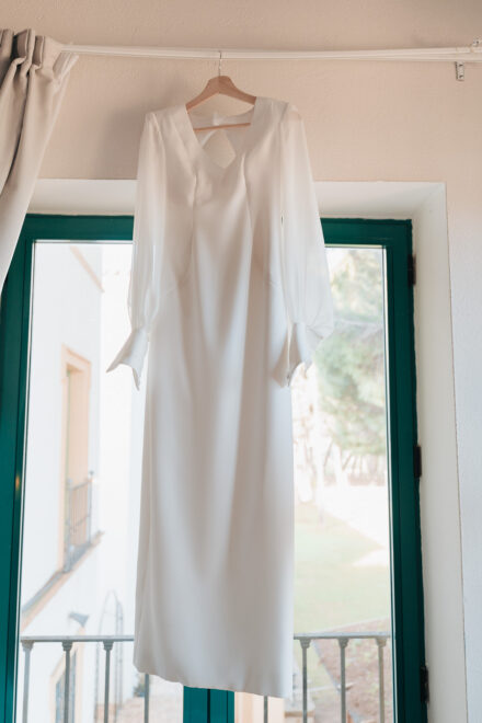 The bride’s long-sleeved dress hanging on a hanger in front of the window
