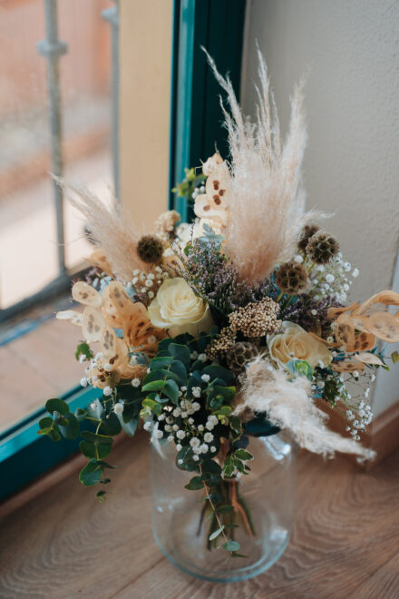 The bride’s bouquet of white roses, eucalyptus, pampas grass and honesty in a vase by the window