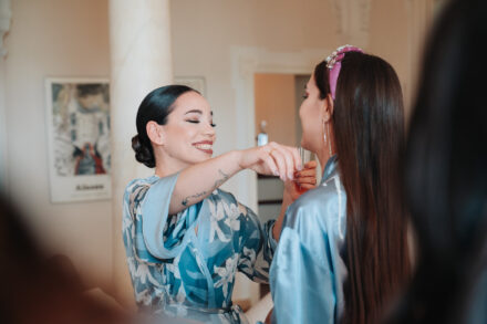 The bride smiles with her eyes closed, reaching toward the face of a guest in a pink headband