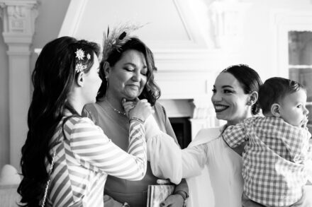 In black and white, a guest strokes the face of an emotional woman while the bride, holding the baby, smiles