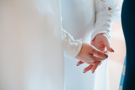 Close-up of the bride’s clasped hands and the buttoned cuffs of her dress