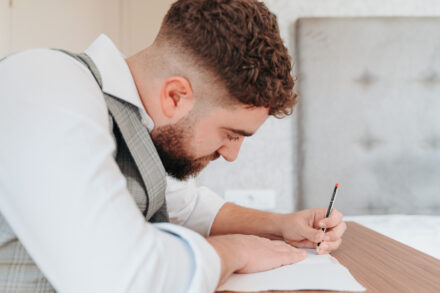 The groom, in a checked waistcoat, writes on a sheet of paper with a pencil while getting ready