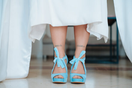 The bride’s feet in blue bow sandals, with a name tattooed on each ankle