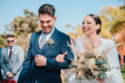 The bride and the young man in the navy suit burst out laughing as they walk arm in arm to the altar