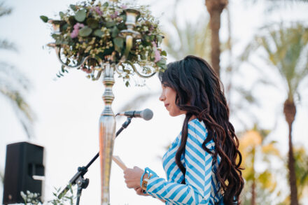 A guest in a blue striped dress reads at the microphone beside a candelabra decorated with flowers