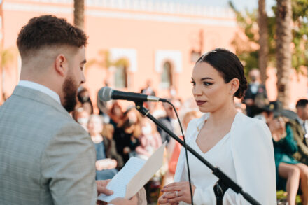The groom reads his vows from a sheet of paper while the bride listens intently at the microphone