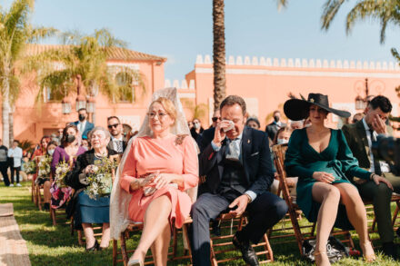 A guest in a white mantilla beside another guest wiping away tears with a handkerchief during the ceremony