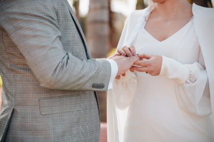 Close-up of the bride's hands slipping the ring onto the groom's finger, him in a grey check suit