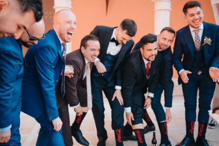 A group of guests in suits bend over laughing to show off their black socks with red lettering