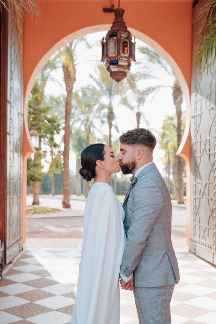 The couple kiss with their eyes closed under a horseshoe arch with a coloured-glass lantern