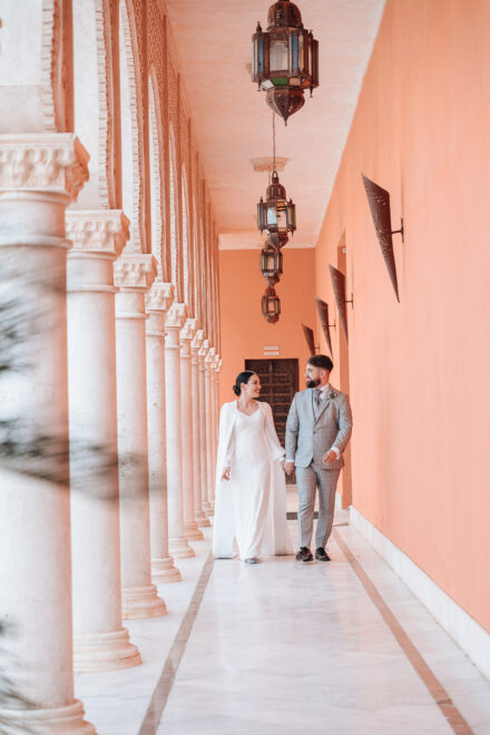 The couple stroll hand in hand along a gallery of white columns and Moorish-style lanterns