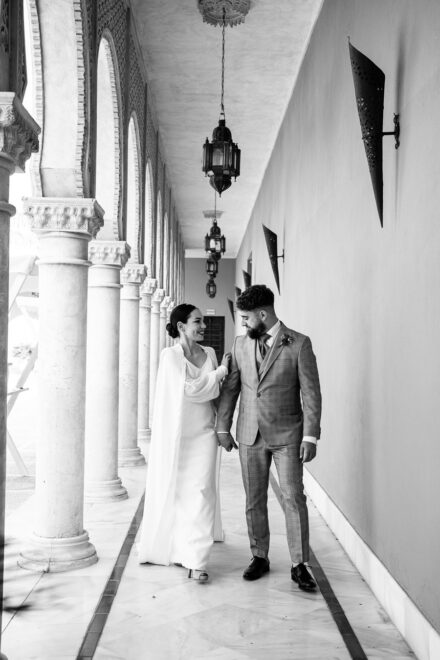 In black and white, the couple walk along the colonnaded gallery, smiling at each other