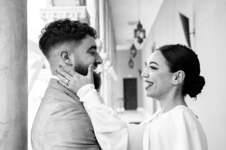 In black and white, the bride cups the groom's face and smiles at him in the gallery