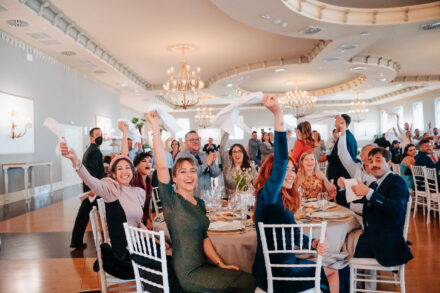 Guests wave white napkins in the air in the banquet hall, under crystal chandeliers