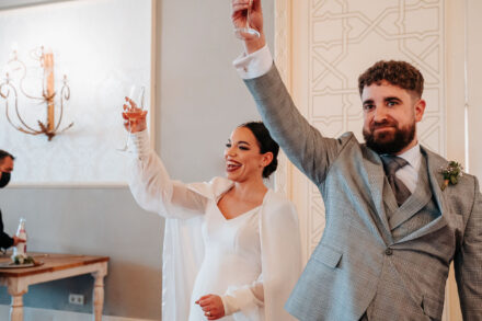 The couple raise their glasses high and smile in the banquet hall