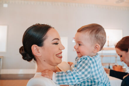 The bride smiles face to face with a baby in a blue gingham shirt, at Hacienda Al-Baraka (Seville)